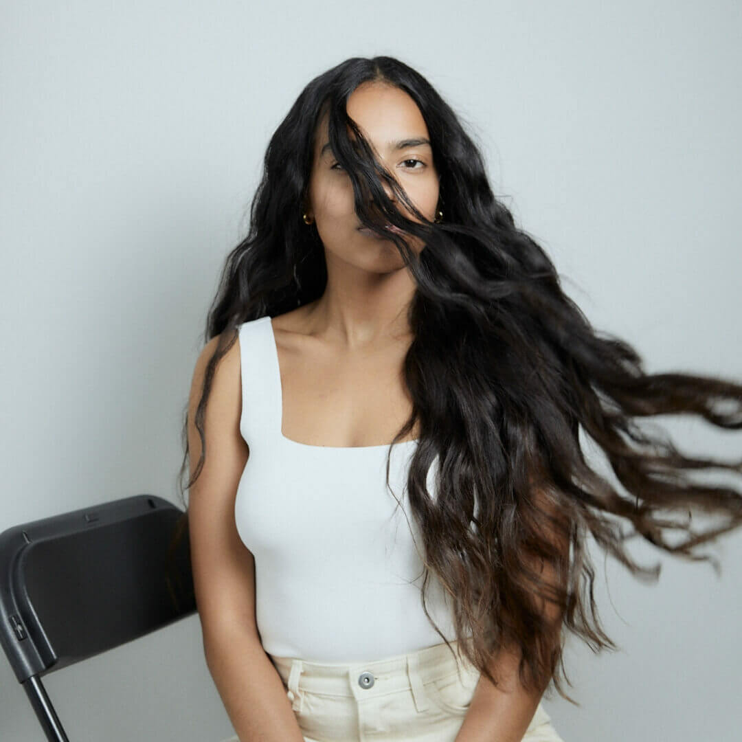 A smiling woman with long, thick hair parted in the middle showcasing how to get thicker hair through effective haircare and styling practices.